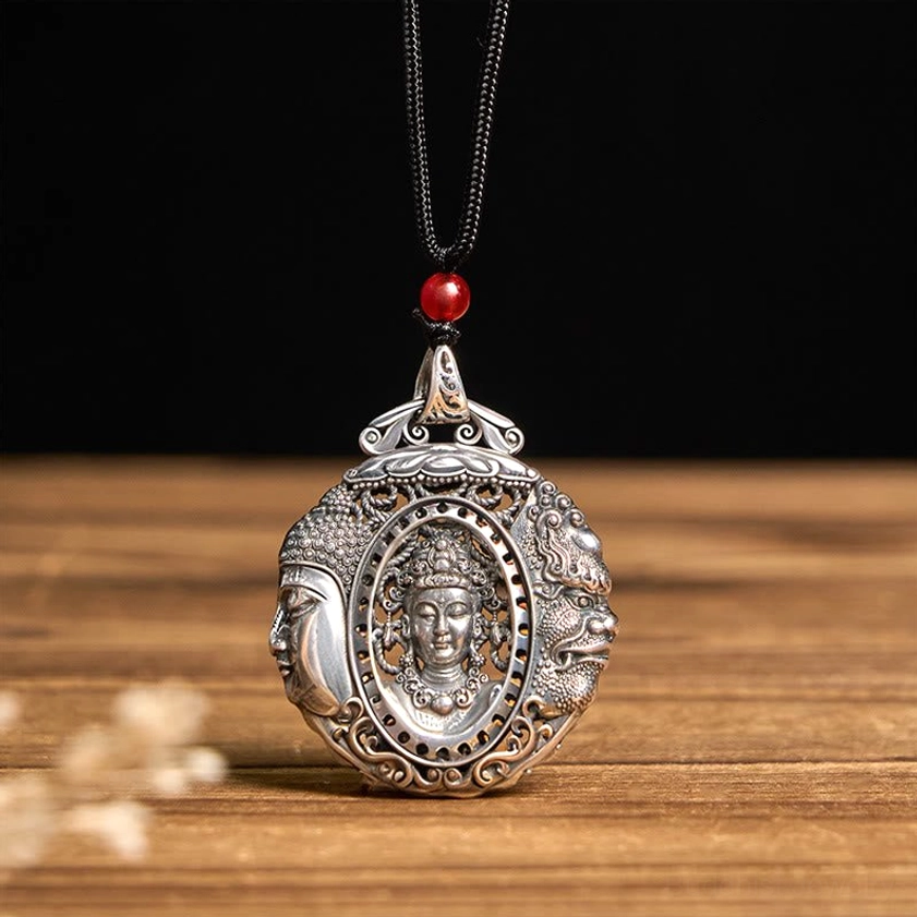 Buddhist pendant necklace with red bead on black woven cord, embossed details on wooden table with flowers
