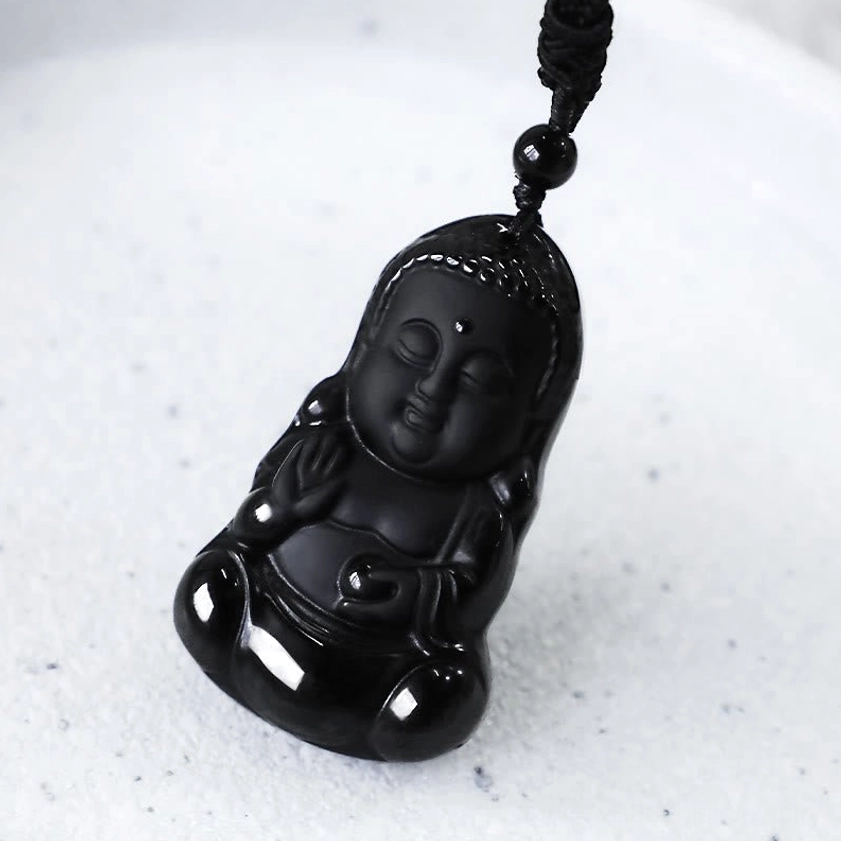 Close-up side view of black obsidian Buddha pendant showing carved facial details and cord