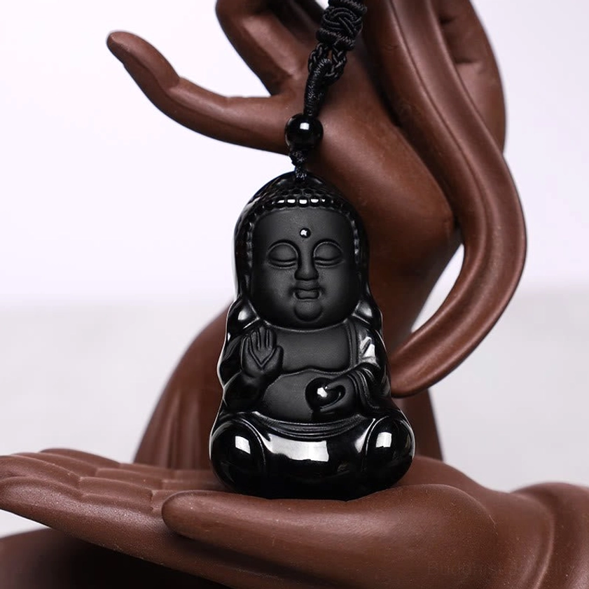 Black obsidian Buddha necklace displayed on decorative ceramic Buddha hand prop - three-quarter view