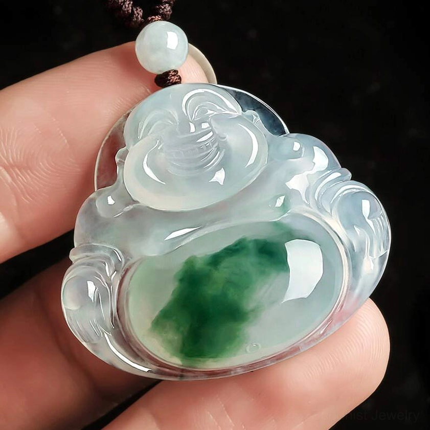 Cyan jade Buddha necklace held in human fingers showing icy jade texture with dark green streaks and brown cord with jade bead accent