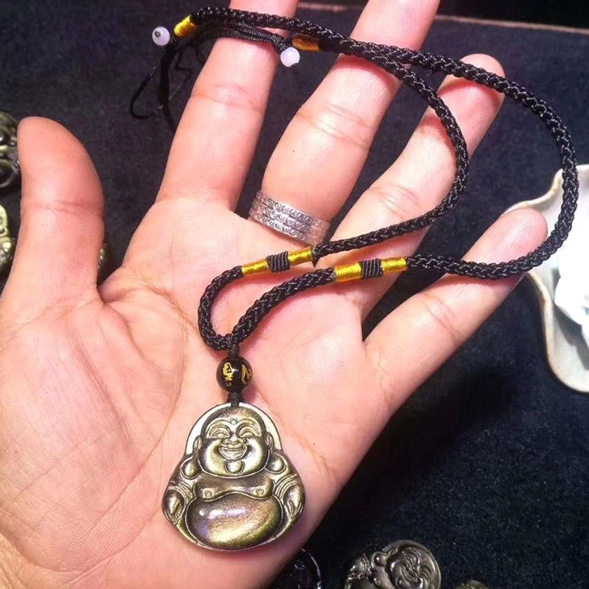 Single laughing Buddha obsidian pendant necklace held in palm showing size scale with woven black cord and golden accent beads