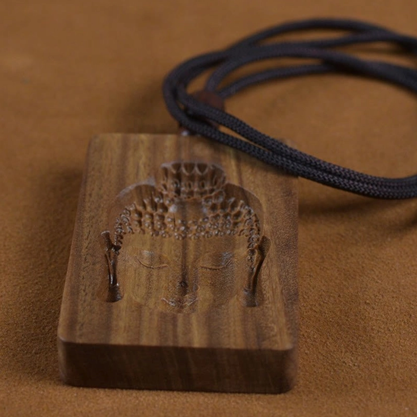 Front low angle view of carved green sandalwood Buddha pendant showing detailed Buddha face relief with natural wood color and black rope necklace