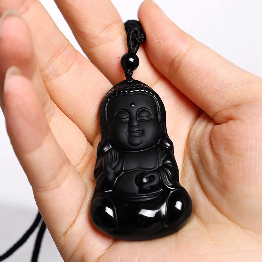 Black obsidian Buddha pendant held in human palm showing actual size and scale