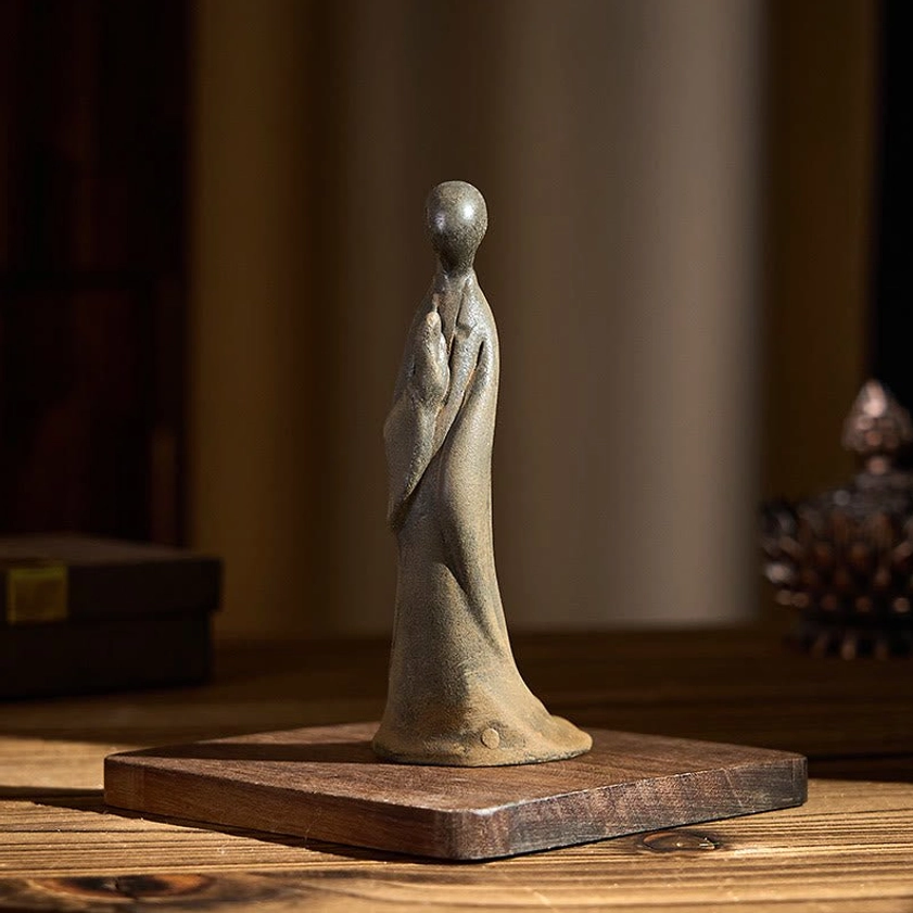 Front angle of handmade Buddha statue on square wooden platform, showing praying hands position and weathered finish