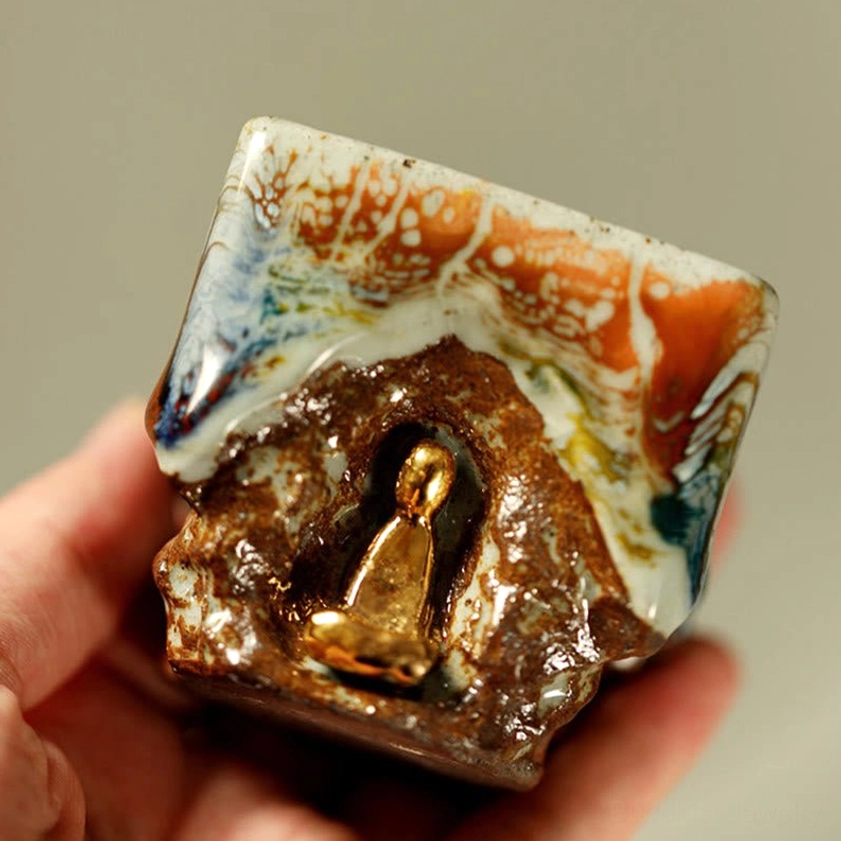 Hand-painted square Shino ceramic Buddha teacup held in hand, showing cave-style relief with gilded meditating Buddha and mixed glaze rim detail