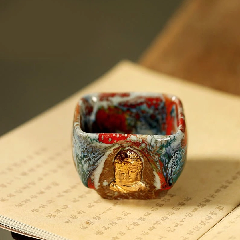 Front overhead close-up view of Dunhuang Buddha teacup showing full gilded Buddha bust relief and multicolor rim glaze on calligraphy background