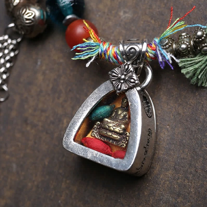 Close-up of silver Buddha shrine pendant with inner Buddha statue and colorful tassel accents on Buddhist bracelet