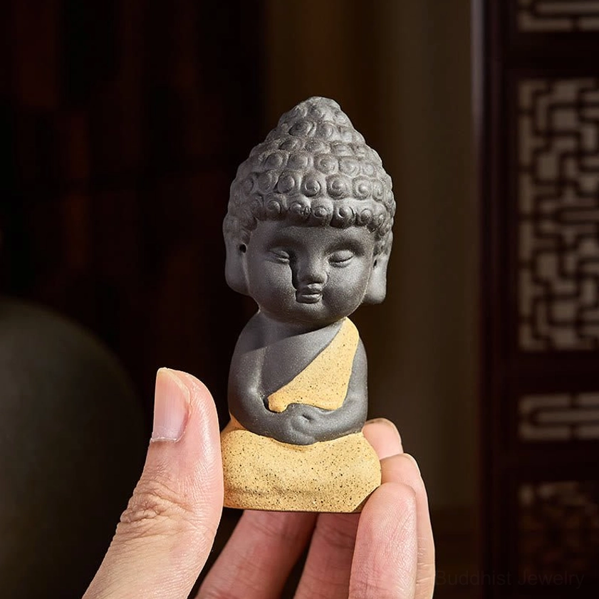 Handcrafted purple clay Buddha statue held in human hand, close-up showing matte natural finish and detail