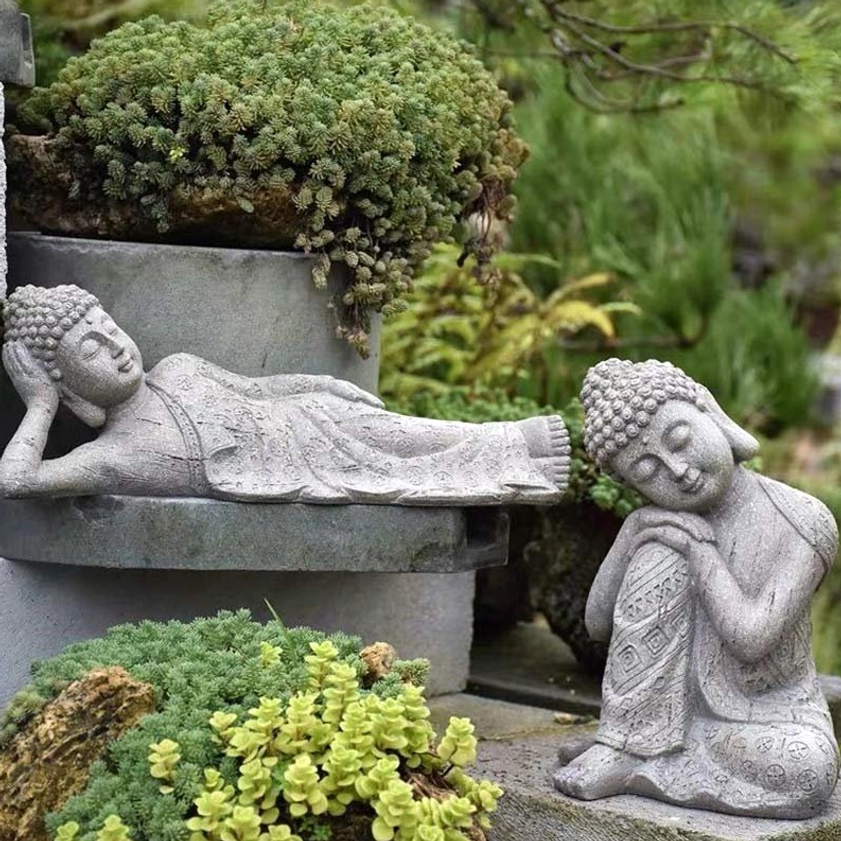 Reclining and seated Buddha figurines displayed together on garden shelf with succulent plants and greenery