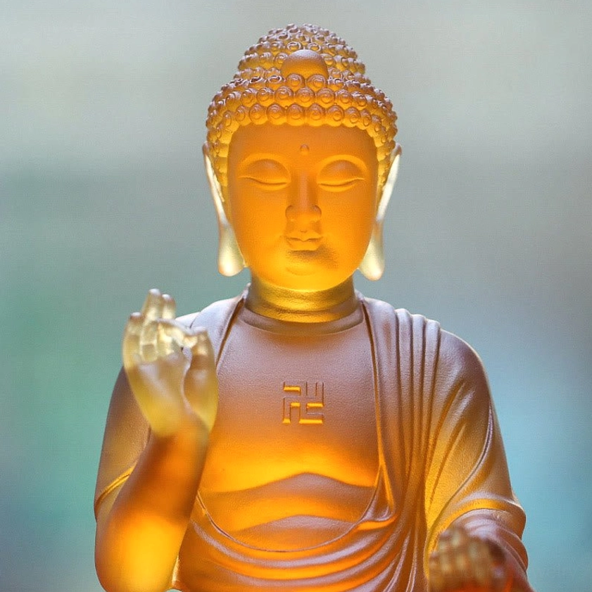 Close-up of Sakyamuni Buddha Liuli statue showing facial features, ear ornaments, blessing hand mudra, and translucent crystal detail
