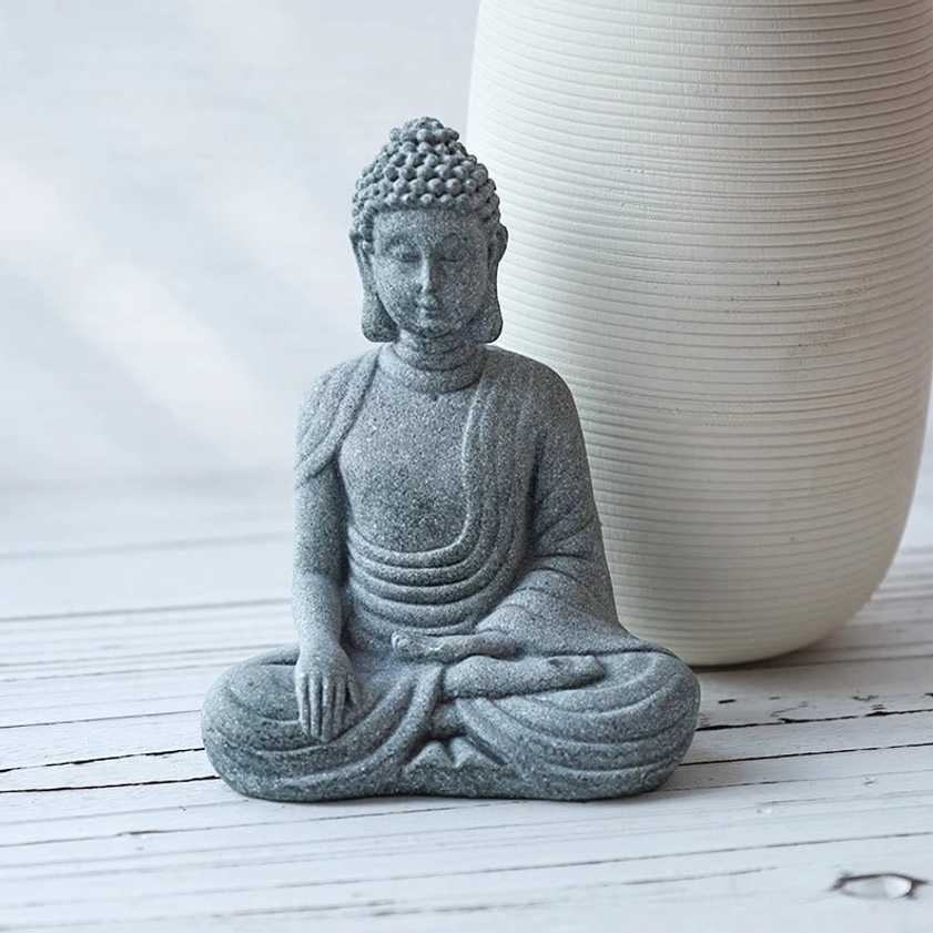 Natural sandstone Buddha statue on wooden tabletop beside ribbed white ceramic vase, oblique angle spiritual home decor view