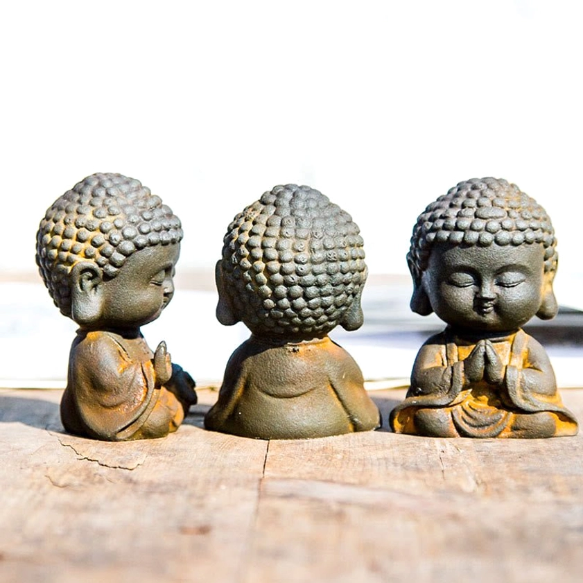 Close-up detail view of iron resin Buddha figurines showing rustic weathered bronze finish with yellow monk robes and curled hair buns