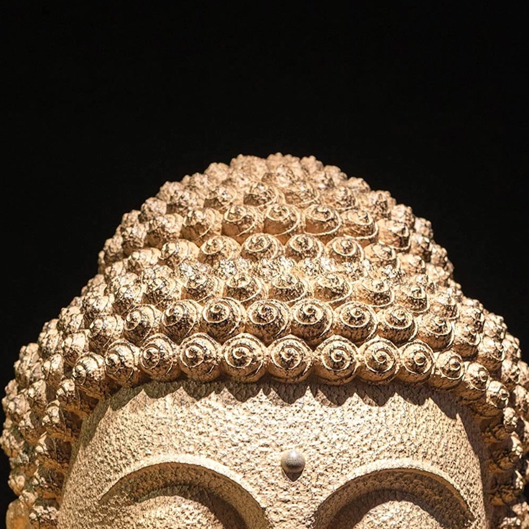 Top view close-up of meditating Buddha head showing detailed carved circular hair bun patterns in tan resin
