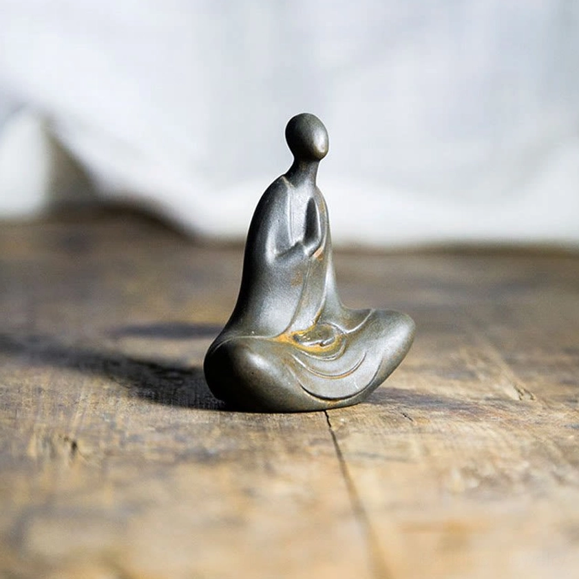 Hand-cast Buddha sculpture in gunmetal gray with rusty accents shown from three-quarter angle on vintage wooden table