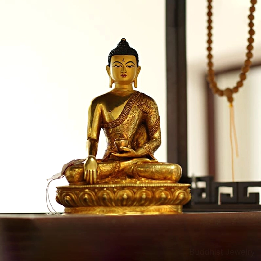Gilt bronze Buddha statue with lotus base in home altar setting surrounded by prayer beads and spiritual décor