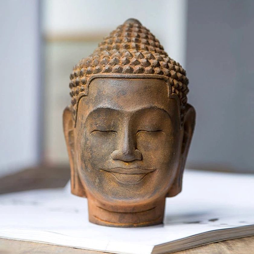 Buddhist meditation head sculpture displayed on open book, showcasing weathered rust patina and detailed facial features