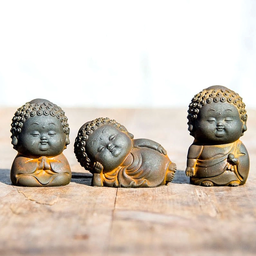 Three mini Buddha figurines with matte rustic finish and worn brown patina edges displayed on natural wood surface