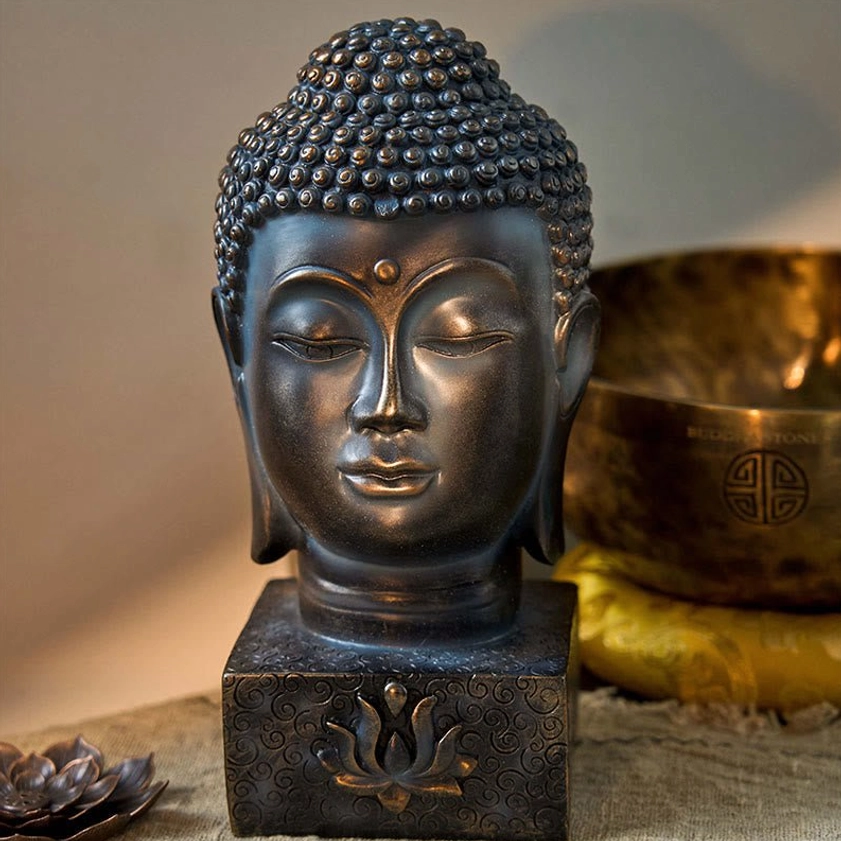 Buddha head decorative statue front view with warm dark bronze tone, lotus base, displayed on tabletop with singing bowl