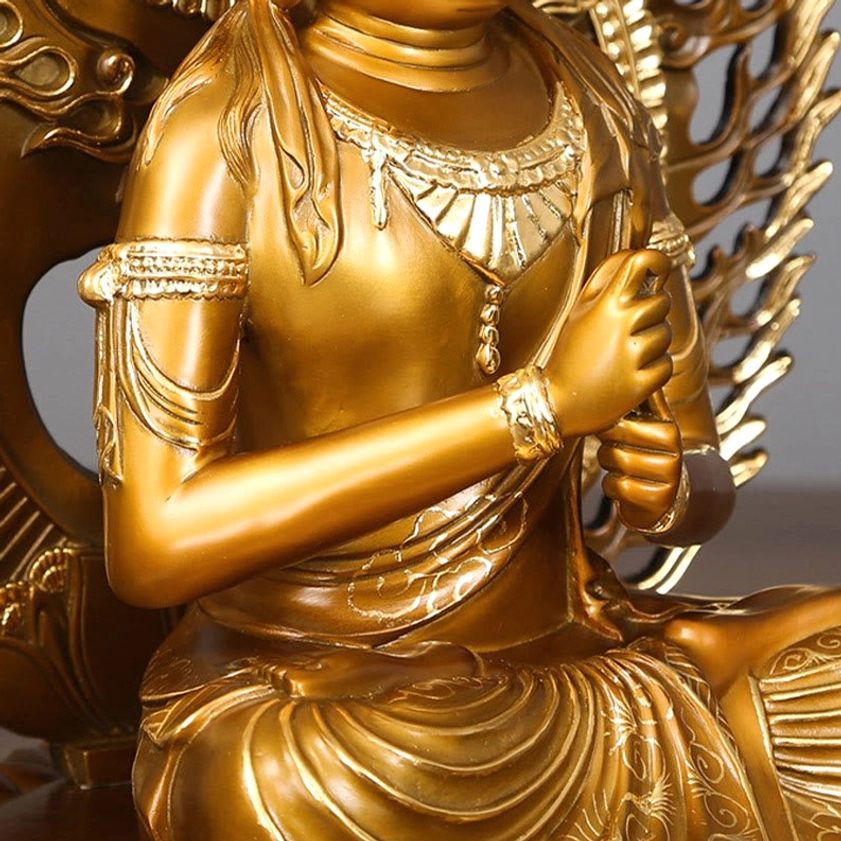 Close-up of Buddha copper statue left side torso showing embossed robe patterns and arm bracelets with golden metallic texture