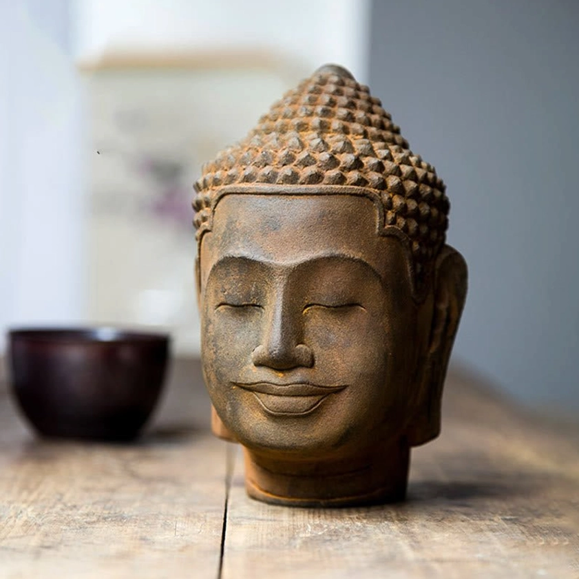 Meditating Buddha head displayed on wooden table next to decorative dark bowl, showcasing mindfulness meditation decor setup