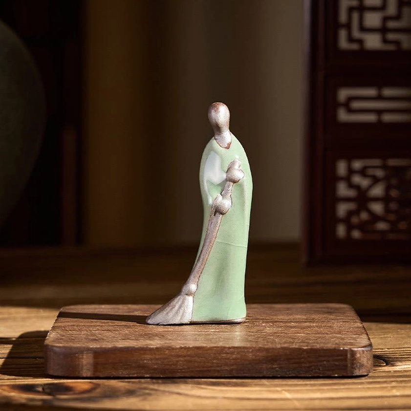 Handcrafted Buddha ceramic figurine rear left angle displayed on wooden table with decorative coaster and Chinese screen backdrop
