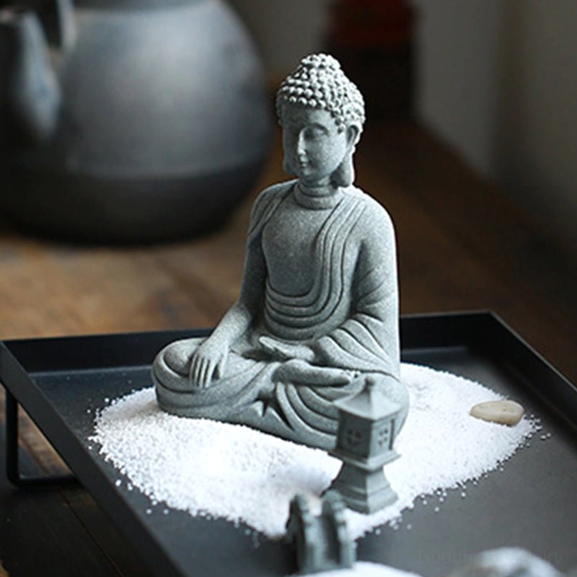 Grey stone finish Buddha meditation statue in zen garden setting with sand tray and mini lantern, detailed robe carving visible