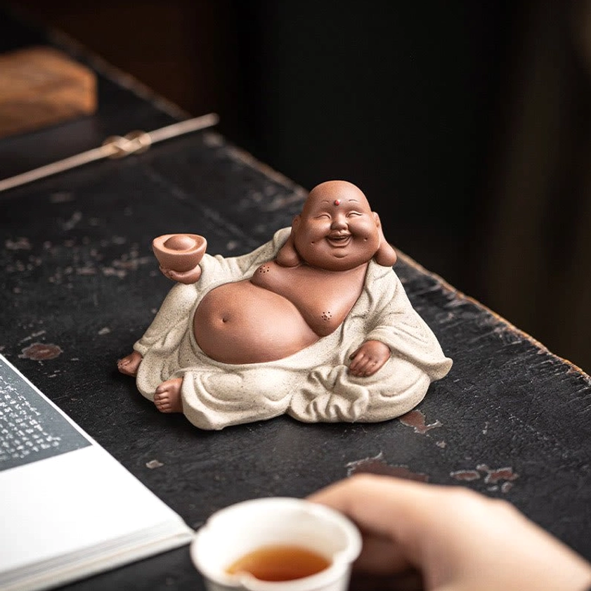 Maitreya Buddha statue positioned on tea table with book and tea cup, right front view, beige ceramic robe, prosperity focal point