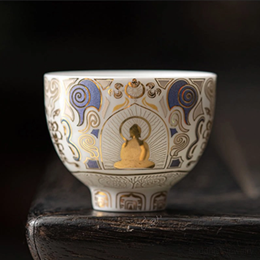 Front-facing white porcelain Buddhist tea cup featuring central gilded Buddha figure with vintage auspicious cloud patterns, displayed on wooden surface