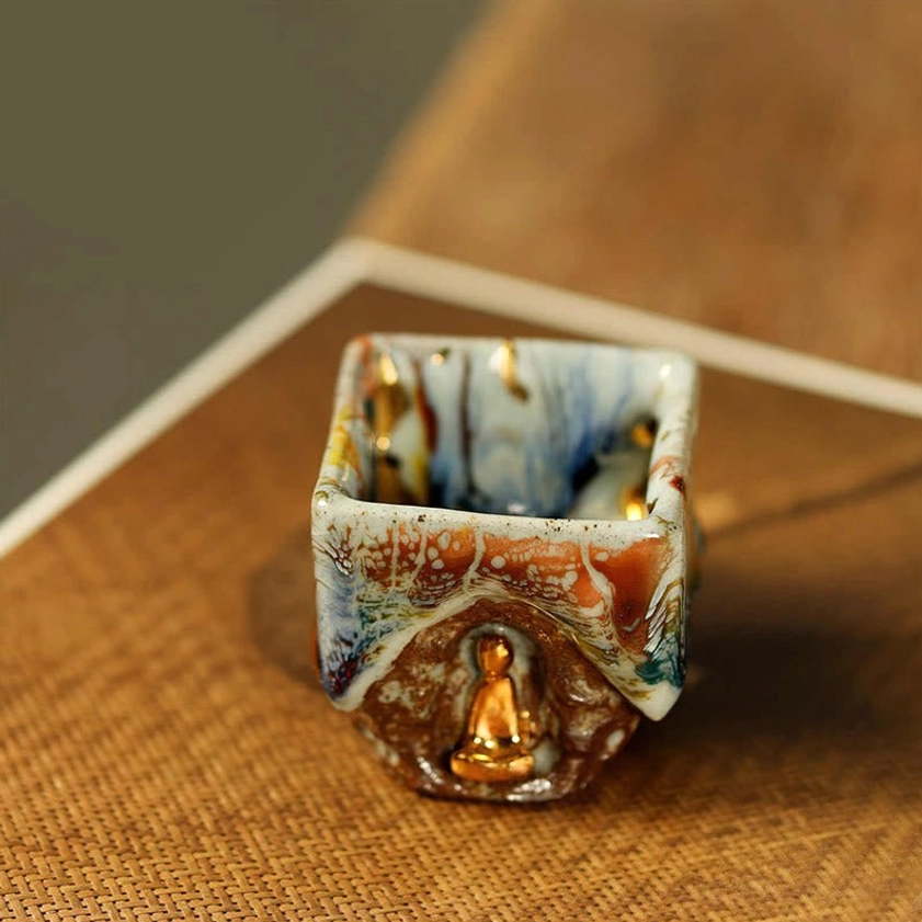 Dunhuang Buddha teacup high side angle view placed on linen and calligraphy paper showing visible glazed interior and gilded seated Buddha on front