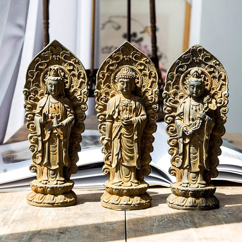 Three-piece Buddhist trinity statue set featuring Amitabha Buddha, Guanyin bodhisattva and Mahasthamaprapta with weathered bronze finish, displayed with spiritual book on wooden surface