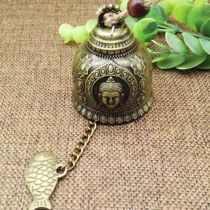 Close-up Buddha embossed wind chime with fish charm on linen fabric with green foliage