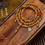 108-bead Buddhist prayer mala with hand-painted Dzi beads, bone barrel beads, turquoise and red accents, silver guru bead and tassel on wooden surface