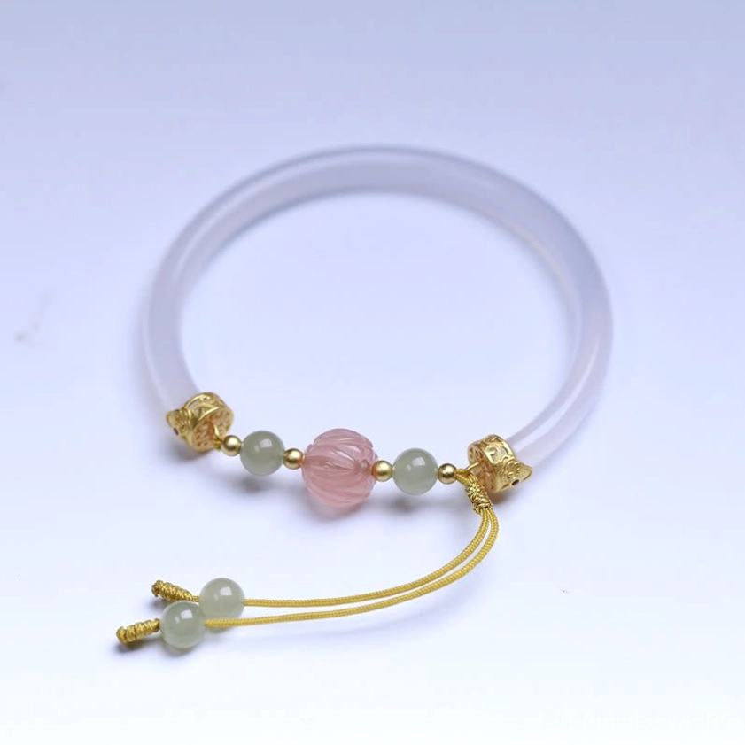 Complete view of white agate Buddhist lotus bracelet with gold-plated silver findings against light blue background