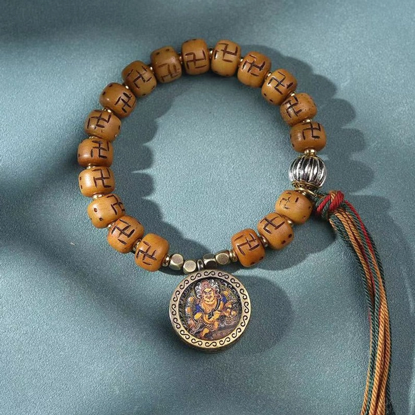 Buddhist amulet prayer bracelet with tan bone beads, metal spacers, ornate Buddha amulet, and woven tassel