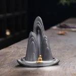 Buddhist mountain backflow incense burner with meditation monk figurine - front view on wooden table