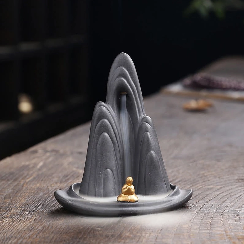 Buddhist mountain backflow incense burner with meditation monk figurine - front view on wooden table