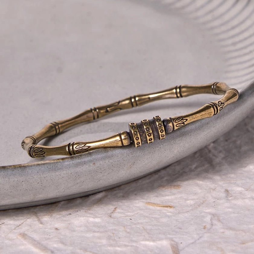 Buddhist bamboo lotus bracelet bangle with multi-ring central decor and intricate lotus motifs, photographed from oblique angle on textured ceramic plate background