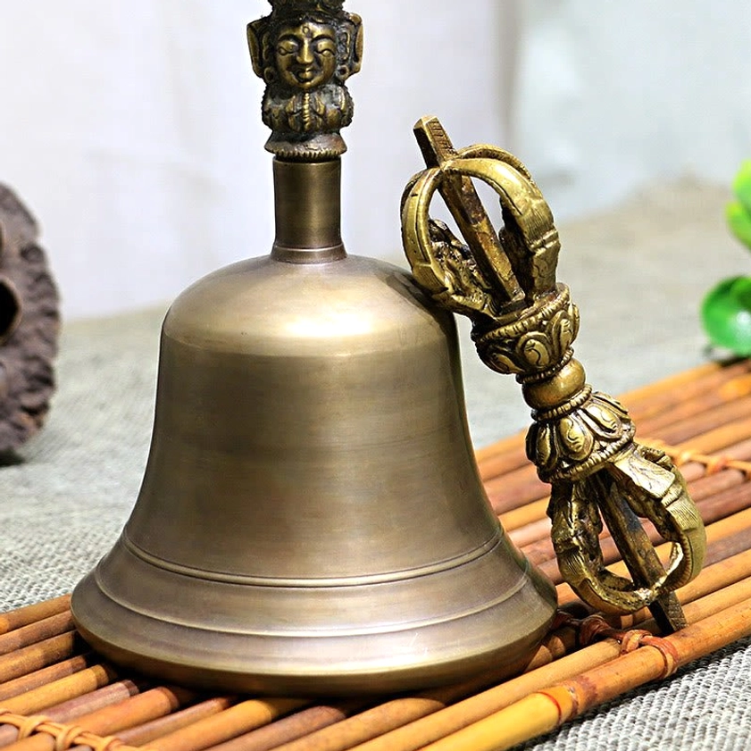 Antique bronze meditation bell and vajra set frontal view on bamboo mat, showing carved Buddha face detail on bell handle