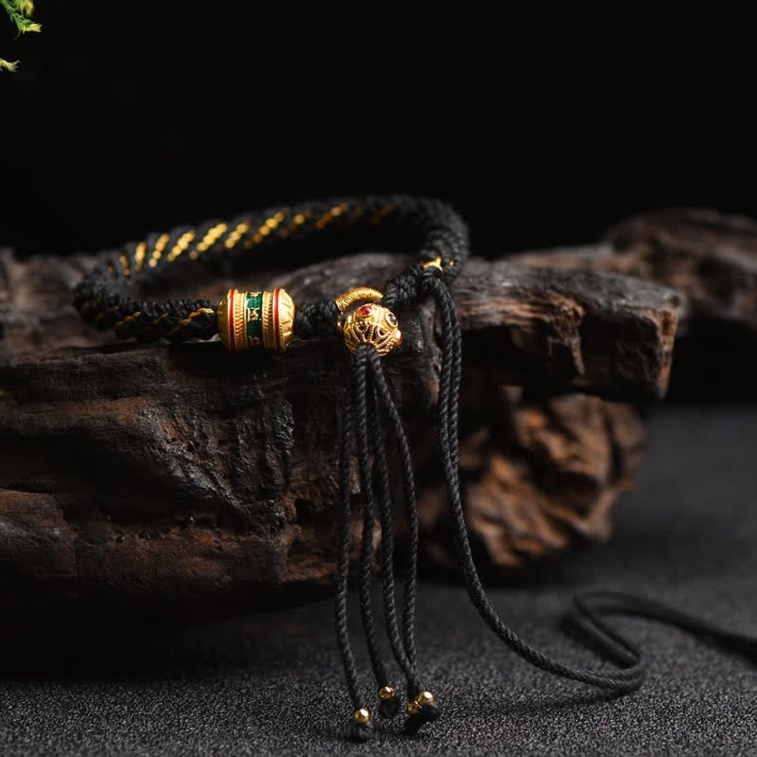 Black Buddhist braided lucky bracelet with gold mixed woven rope and prayer wheel charm on rustic wood