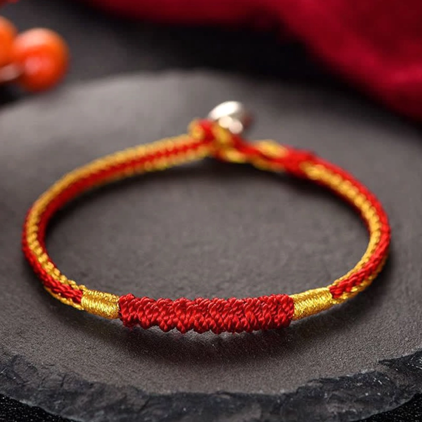 Red and gold handmade braided Buddhist protection bracelet with prominent woven section and metal clasp on white background