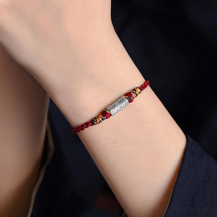 Buddhist blessing bracelet with everything goes well design, showing silver tube charm and braided rope construction from side angle