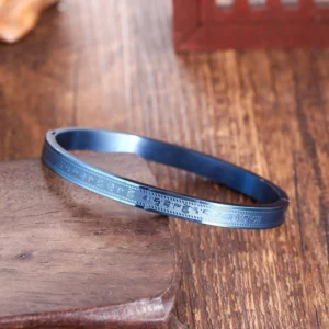 Titanium steel Buddhist blessing bracelet with burnt blue finish and engraved scripture patterns, displayed on wooden base from top-down angle