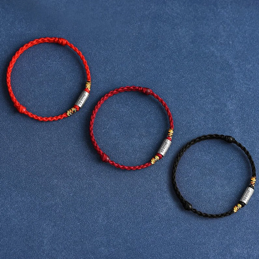 Collection of three Buddhist string bracelets with various rope colors - red, black, and rainbow - featuring sterling silver charms with spiritual characters, flat lay display