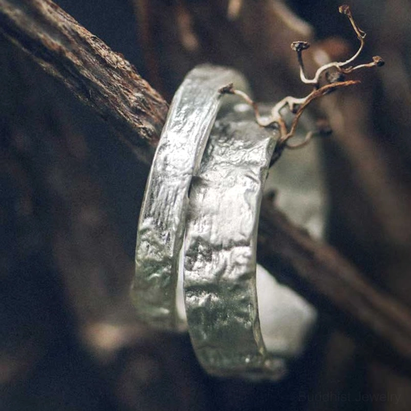 Two textured silver rings with rough hammered finish hanging display on natural wood background