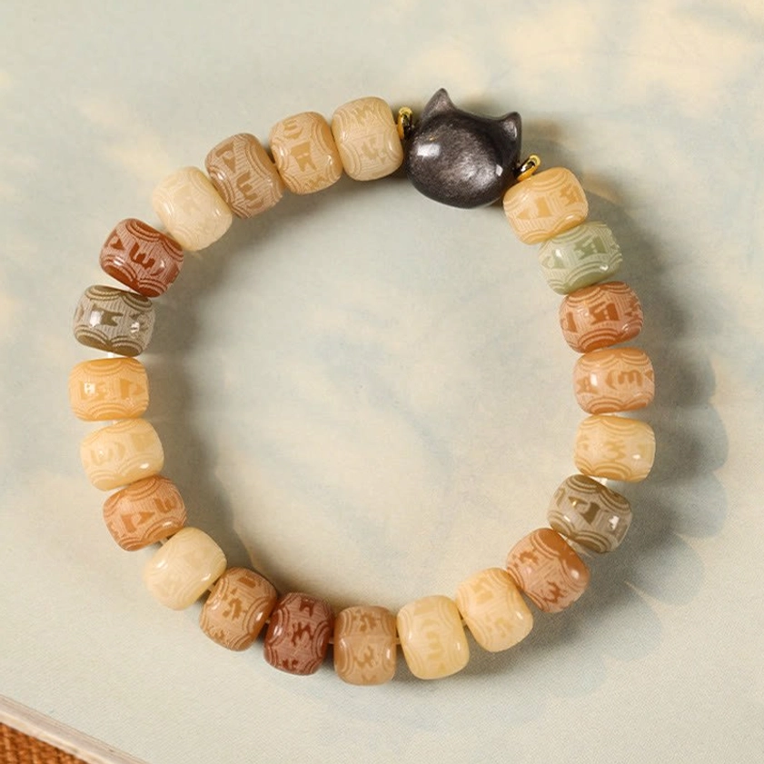 Sacred bodhi seed bracelet with obsidian cat charm, full overhead flat lay on white paper showing bead details