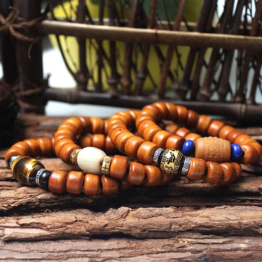 Multiple Buddhist bone bead bracelets with various metal charms and colored spacers on wooden display