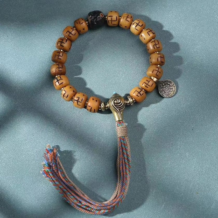 Minimalist Buddhist bone bead bracelet with metal toggle clasp, round pendant, and woven tassel on fabric