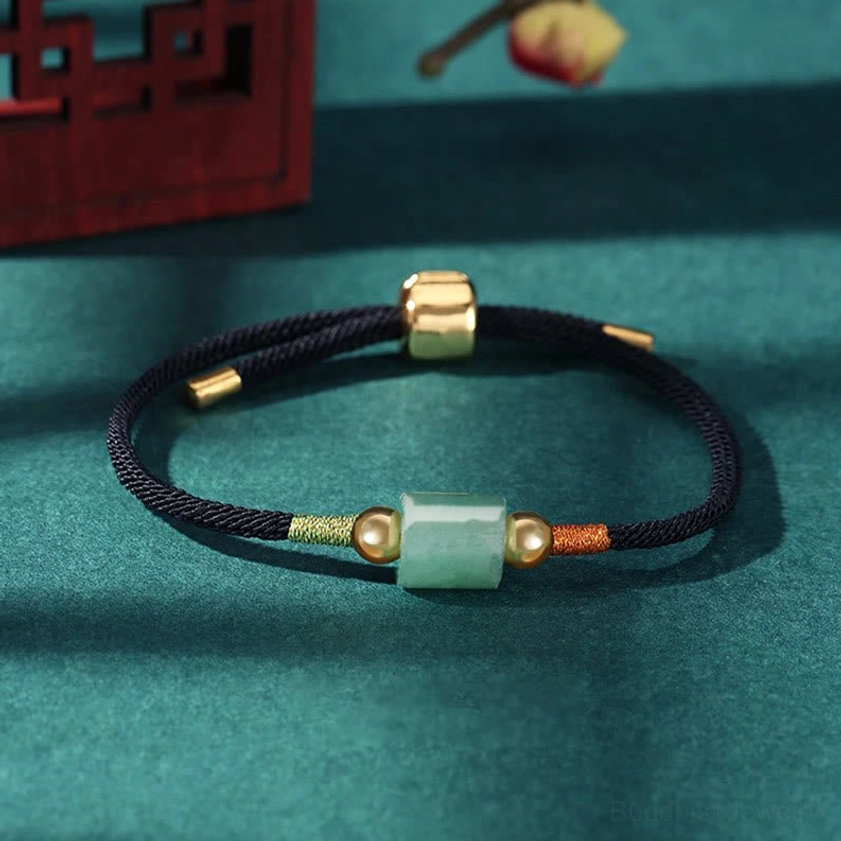 Black braided rope Buddhist string bracelet with green aventurine stone charm and gold metal accents on teal Chinese desktop