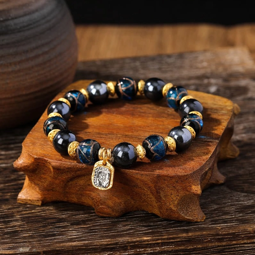 Close-up detail of navy blue Buddhist wealth bracelet with glossy Liuli glass beads and square engraved prosperity pendant