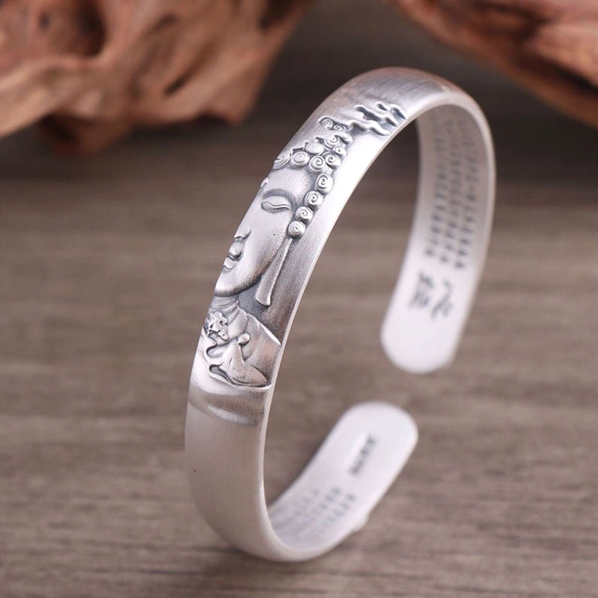 High-relief embossed Buddha face on sterling silver cuff bracelet, front close-up detail showing sutra engravings and polished silver edges